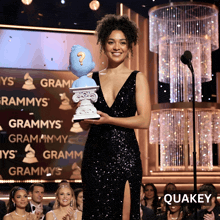 a woman in a black sequined dress is holding a trophy in front of a sign that says grammys