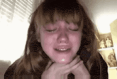 a young girl is crying with her eyes closed while holding her neck .