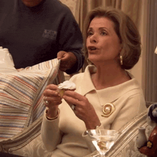 a woman sitting on a couch with a martini glass and a cupcake in her hand