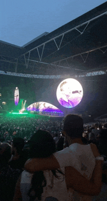 a man and a woman are hugging in front of a huge screen at a concert