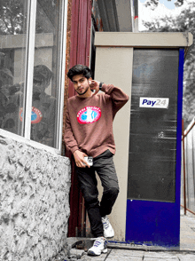 a man leaning against a wall with a pay24 sign behind him