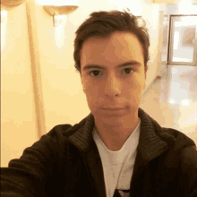 a young man taking a selfie in a hallway wearing a black jacket and a white shirt