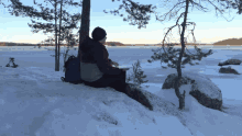 a person sitting on a snow covered rock near a lake with a hoodie that says ' fila ' on it