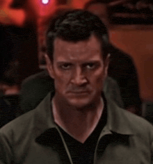 a man in a green jacket looks at the camera with a serious look on his face
