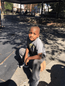 a young boy in a grey shirt sits on a basketball in a park