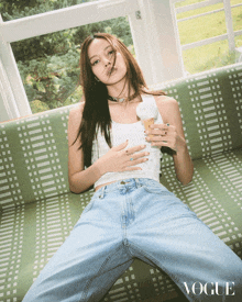 a woman laying on a green couch holding an ice cream cone with the word vogue on the bottom right