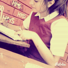 a girl sits at a desk in front of a wall that says hms on it