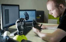 a man is sitting at a desk in front of a computer holding a prosthetic hand .