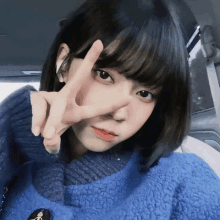 a girl wearing a blue sweater is giving a peace sign