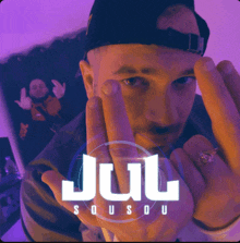 a man wearing a hat and a ring is giving the middle finger in front of the jul logo