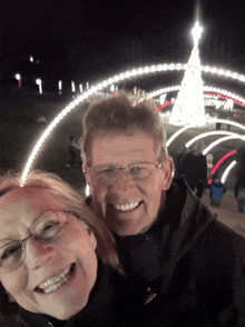 a man and woman smile for a picture in front of a christmas tree