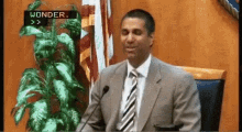 a man in a suit and tie is giving a speech in front of a microphone with wonder written on the screen behind him