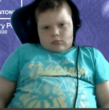 a young boy wearing headphones and a blue shirt is looking at the camera .