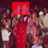 a woman in a red dress is holding a sign in front of a crowd of people at a concert .