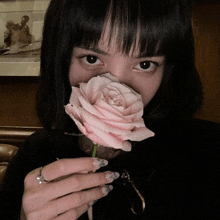 a woman with a ring on her finger is holding a pink rose in front of her face