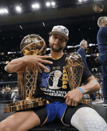 a man in a golden state warriors shirt is holding two trophies