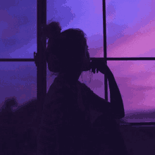 a woman looks out a window at a purple sky