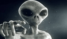 a black and white photo of an alien making a gesture with his hand .