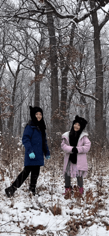 two young girls are standing in the snow wearing hats