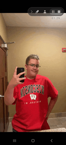 a young man wearing a red wisconsin shirt taking a selfie