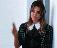 a woman wearing a plaid jacket and a white collar is standing next to a wall .
