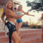 a woman in a bikini is dancing with another woman in shorts