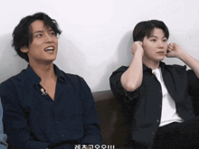 two men are sitting on a couch and one of them has a foreign language written on his shirt