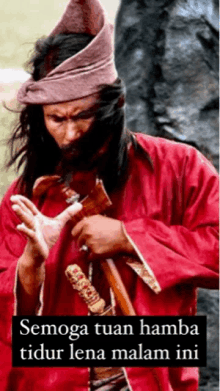 a man in a red robe is holding a sword and wearing a hat