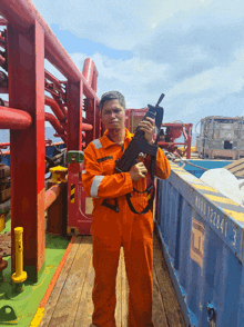 a man in an orange jumpsuit holds a gun in front of a blue container with the number 122844