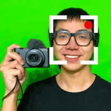 a man in glasses is holding a camera in front of his face .