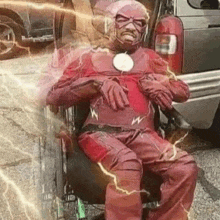 a man in a flash costume is sitting in a wheelchair next to a car .