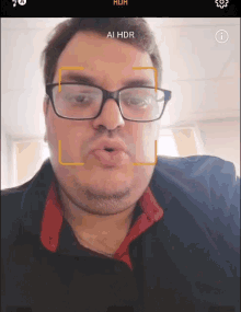 a man wearing glasses is taking a selfie and the screen says ai hdr on it