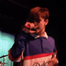 a man is singing into a microphone while wearing a blue red and white shirt with the word dolce on it