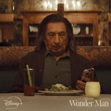 a man is sitting at a table with a plate of food and a glass of orange juice and wonder man is written on the table