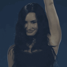 a woman with long dark hair is smiling with her hand in the air