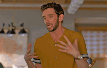 a man in a yellow shirt is saying sorry with his hands on his face