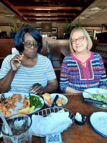 two women sitting at a table with plates of food and a qr code on the table