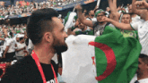 a man wearing a black shirt that says ' a ' on it stands in a crowd holding a flag