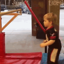 a young boy is playing with a red stick in front of a sign that says ' a ' on it .