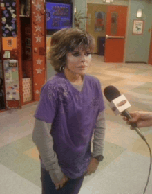 a woman in a purple shirt is being interviewed by a person with a microphone