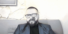 a man with glasses and a beard is sitting on a couch with the word go on his face
