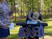 a baby is sitting in a high chair with a cake and a sign that says one