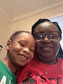 a woman wearing glasses and a red shirt that says sister smiles with a child