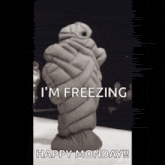 a black and white photo of a statue wrapped in a sleeping bag with the words `` i 'm freezing happy monday ''