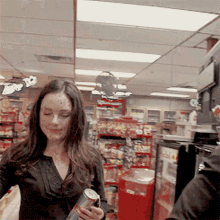 a woman holding a can of soda in a store with a sign that says ' to go ' on it