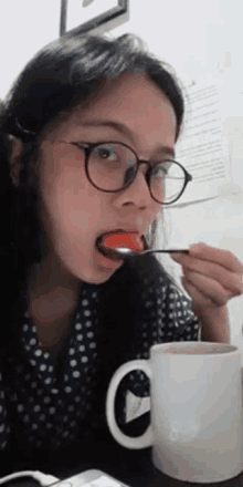 a woman with glasses is eating something with a spoon in her mouth