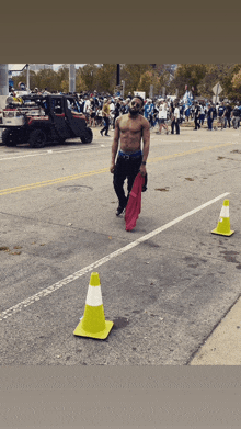 a shirtless man walking down a street with a pink shirt on