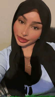 a woman wearing a black hijab and a necklace with the letter r on it