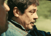 a man with a beard and a denim shirt is talking to another man