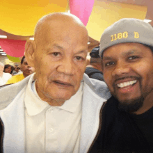 a man wearing a hat with the number 1180 on it poses for a picture with an older man